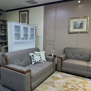Grey upholstered sofa set with dark wood arm accents, high backs and vertically ribbed lower panels.