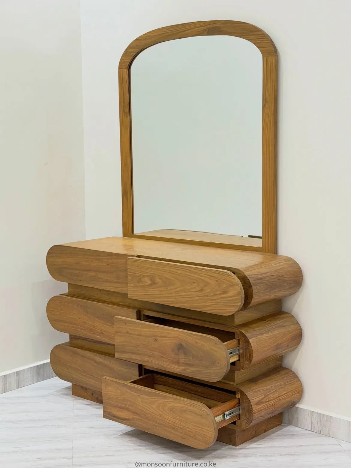 Muninga dressing table with a large framed mirror and six rounded warm-brown drawer fronts arranged in three tiers.