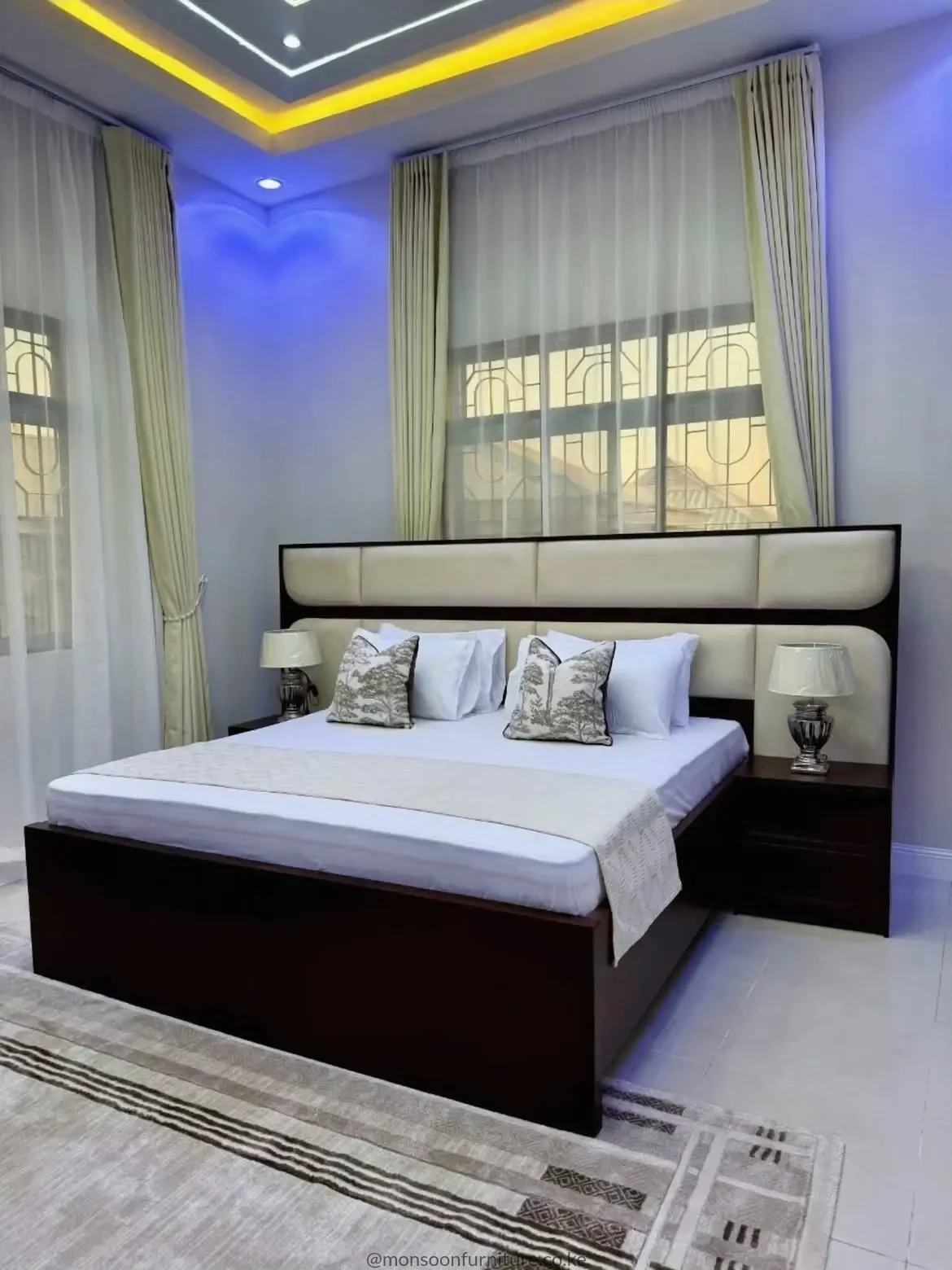 Dark brown bed with wide cream padded panel headboard, low frame and matching bedside cabinets in a bright bedroom.
