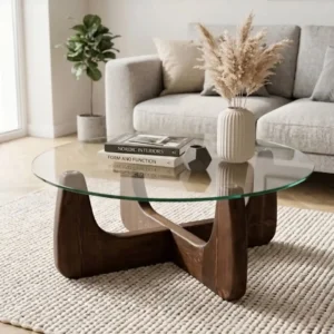 Round clear glass coffee table with sculptural dark wooden base in a neutral modern living room