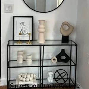 Black small console table with clear glass shelves and round black-framed mirror in a bright hallway