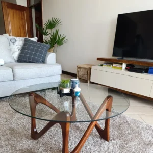 Tara round glass coffee table with sculptural brown mahogany wood base in a living room