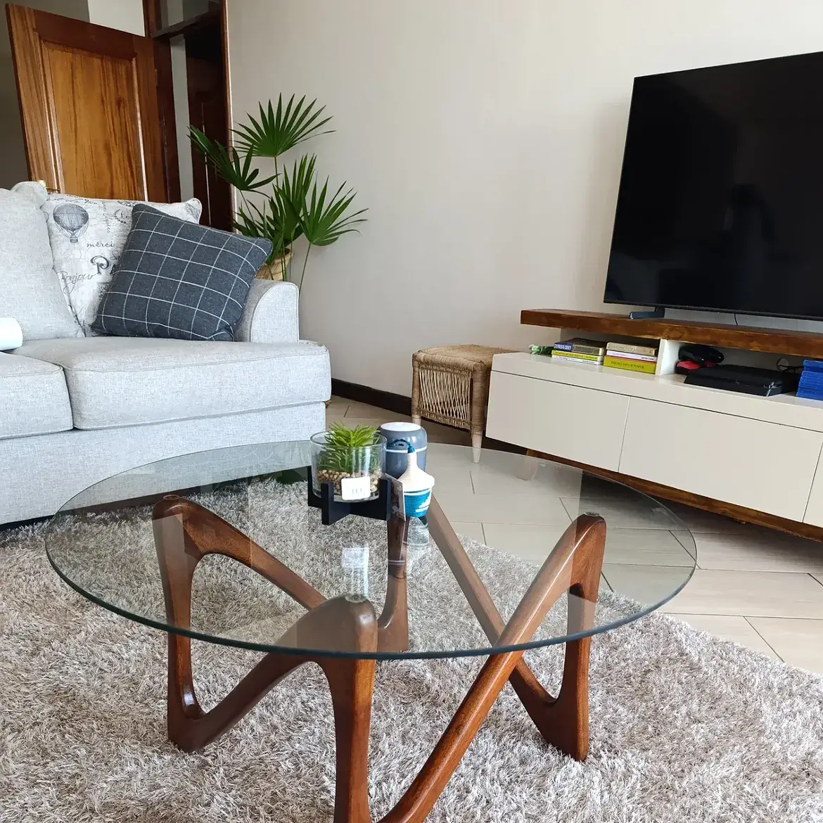 Tara round glass coffee table with sculptural brown mahogany wood base in a living room