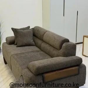 Taupe-brown sofa with textured upholstery, broad padded arms, segmented back cushions and wood-tone side accents in a bright room.