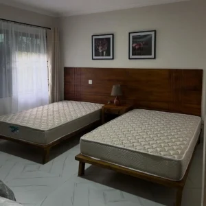 Two 4×6 wooden beds with a wide brown shared headboard and central bedside table in a bedroom