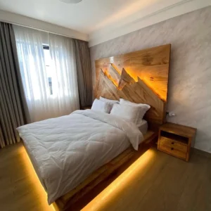 Walnut-look platform bed with illuminated mountain-design headboard and warm under-bed lighting in a modern bedroom