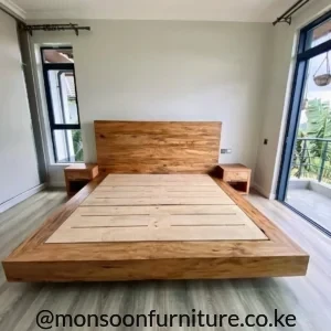 Warm brown wooden platform bed with wide panel headboard, recessed support base and two matching bedside units in a bright bedroom.