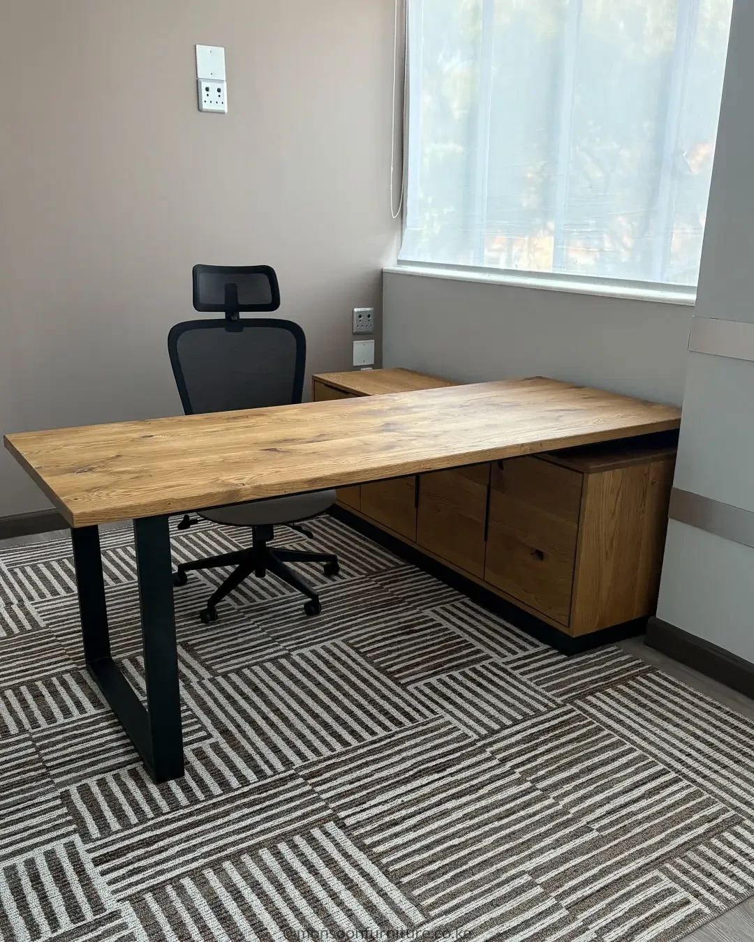 Wood-grain executive office desk with black frame legs and right-side storage in a professional office