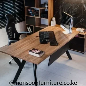 Wood-tone executive office desk with broad rectangular top, black angled legs and dark modesty panel.