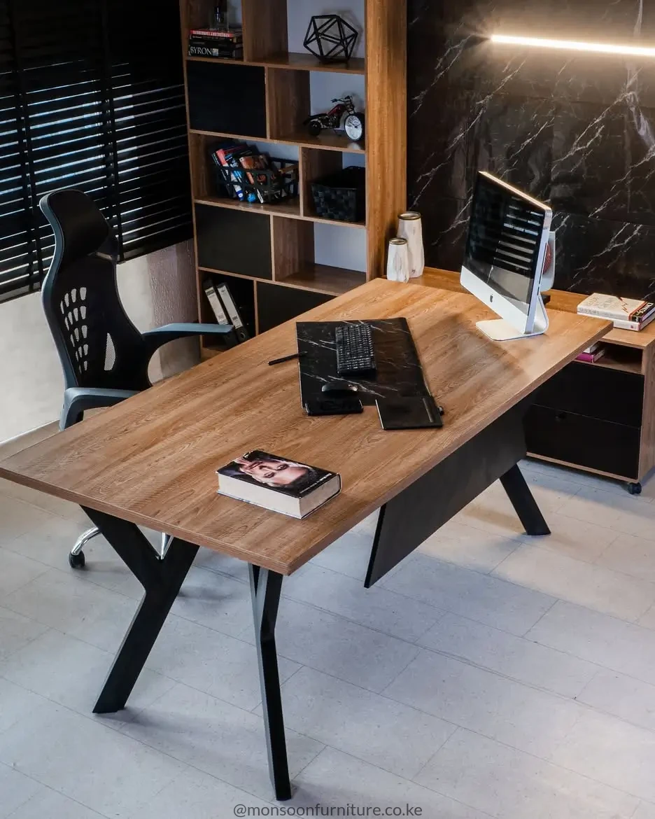 Wood-tone executive office desk with broad rectangular top, black angled legs and dark modesty panel.