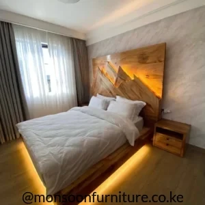 Warm brown wooden platform bed with angular illuminated headboard and warm under-bed lighting beside a two-drawer bedside table.
