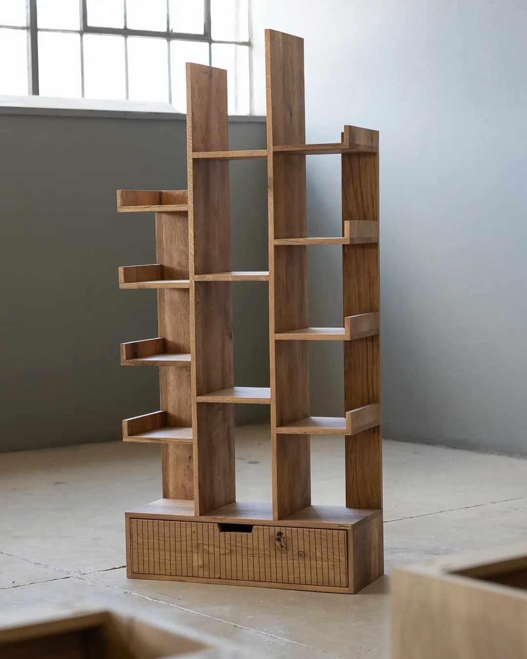 Branton Mvule wood bookshelf with asymmetric open shelves and lower drawer