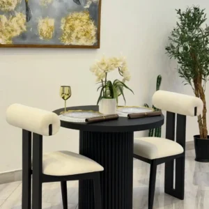 Black round fluted pedestal dining table with two cream upholstered chairs