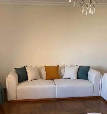 Cream 3 seater sofa with rounded arms, three seat cushions and contrasting scatter cushions in a living room