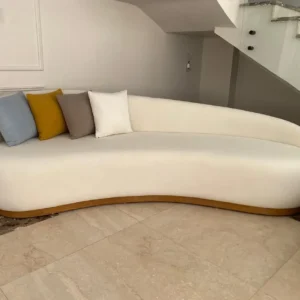 Cream asymmetrical curved sofa with rounded back and wood-toned lower accent