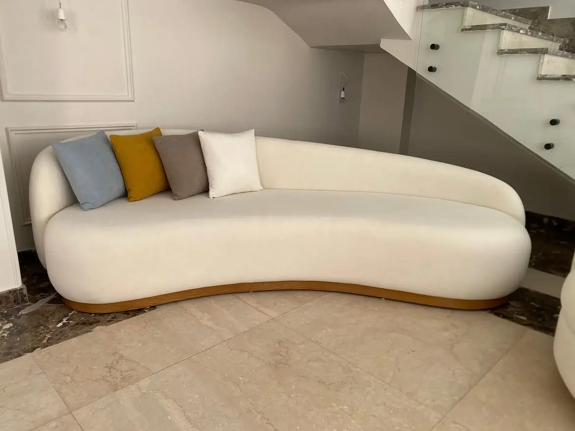 Cream asymmetrical curved sofa with rounded back and wood-toned lower accent