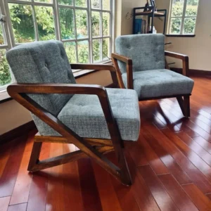 Two grey textured accent chairs with button-tufted backs and exposed dark-finished frames beside a large window