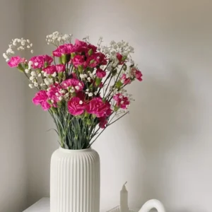 White Nordic ribbed ceramic vase holding bright pink and small white flowers on a white table