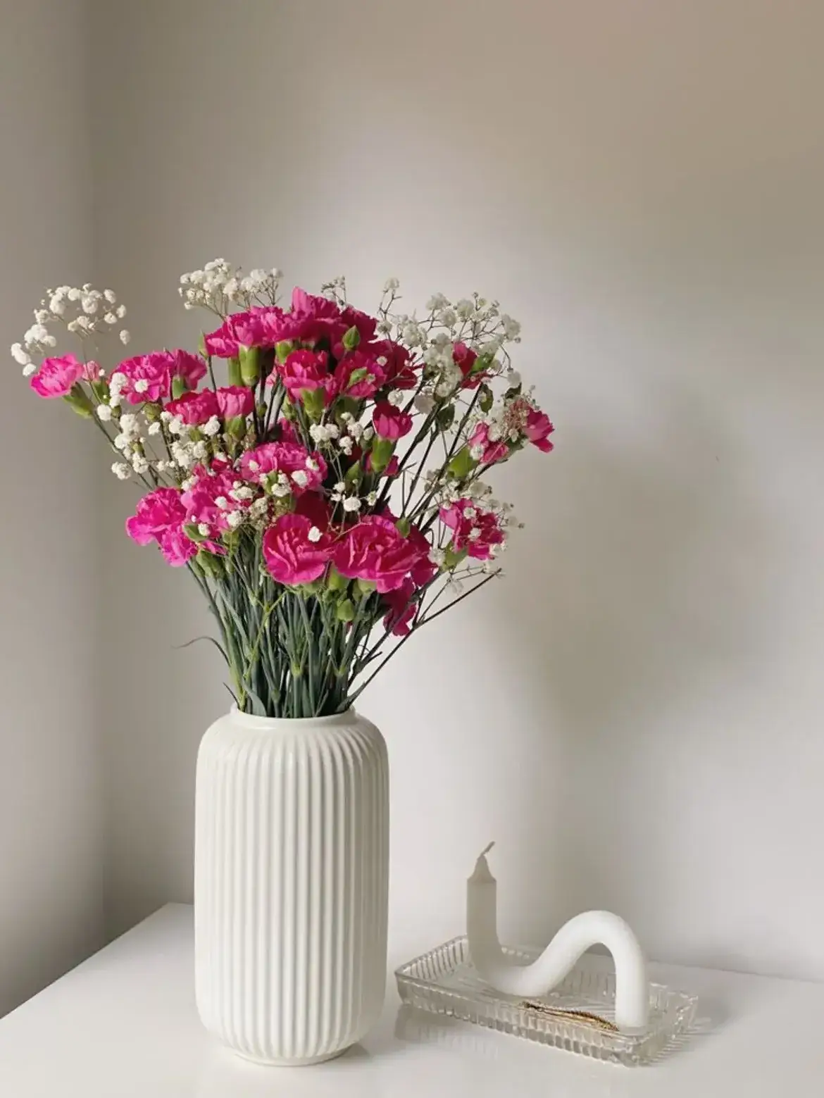 White Nordic ribbed ceramic vase holding bright pink and small white flowers on a white table