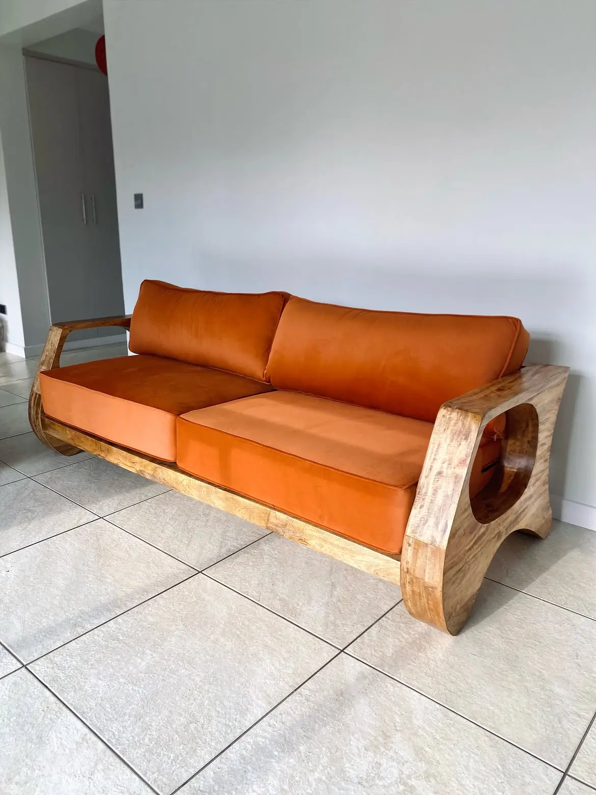 Terracotta upholstered sofa with curved exposed wood frame and oval arm openings in a tiled living room