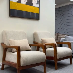 Two cream upholstered wooden lounge chairs with curved brown armrests and angled backs