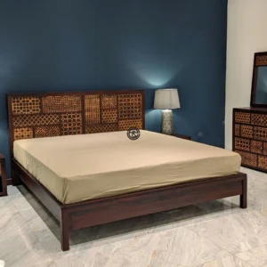 Monsoon Amberborough 6×6 dark-brown wooden bed with mixed geometric patchwork headboard, low footboard and raised supporting legs.