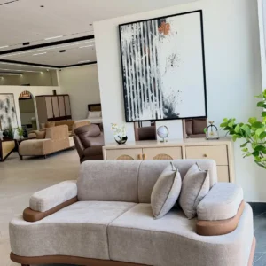 Monsoon Cleargate two-seat sofa in grey-beige textured upholstery with broad rounded armrests, tan-brown trim and matching cushions.